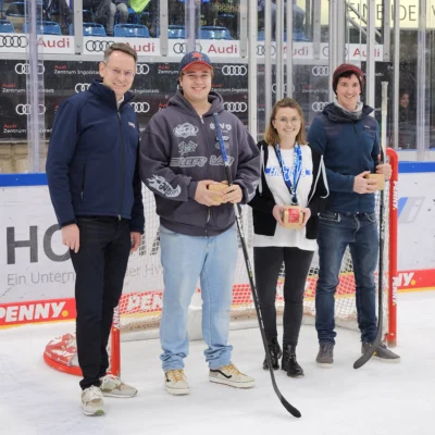 Foto: ERC Ingolstadt Promo Aktion Dezember 2023 - 4 Personen vor Eishockeytor auf dem Eis in der Saturn Arena
