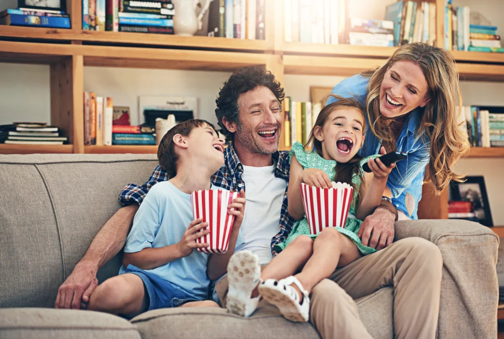 Foto: Glückliche Familie (Sohn, Mann, Tochter, Frau) auf grauer Couch vor hölzernen Bücherregal